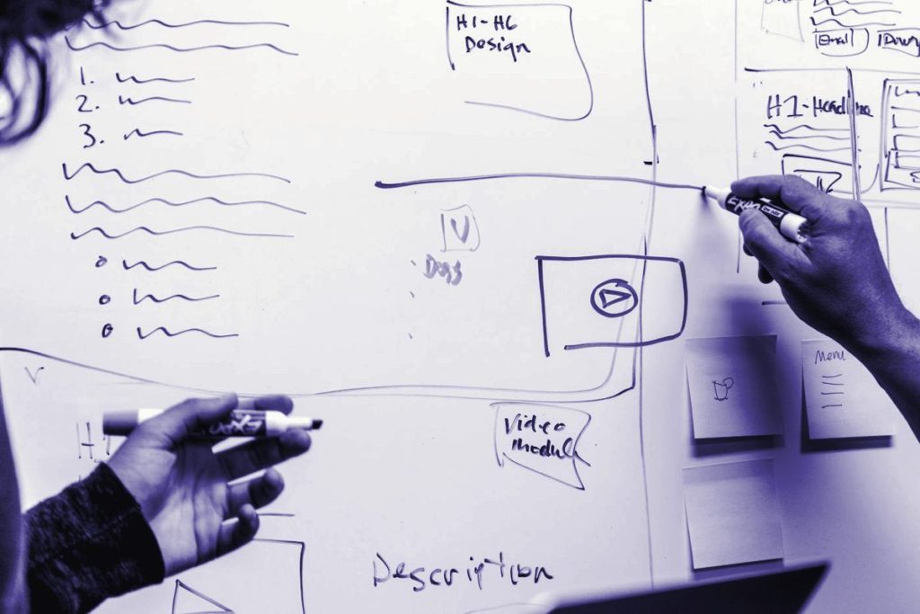 Hands sketching a plan on a whiteboard